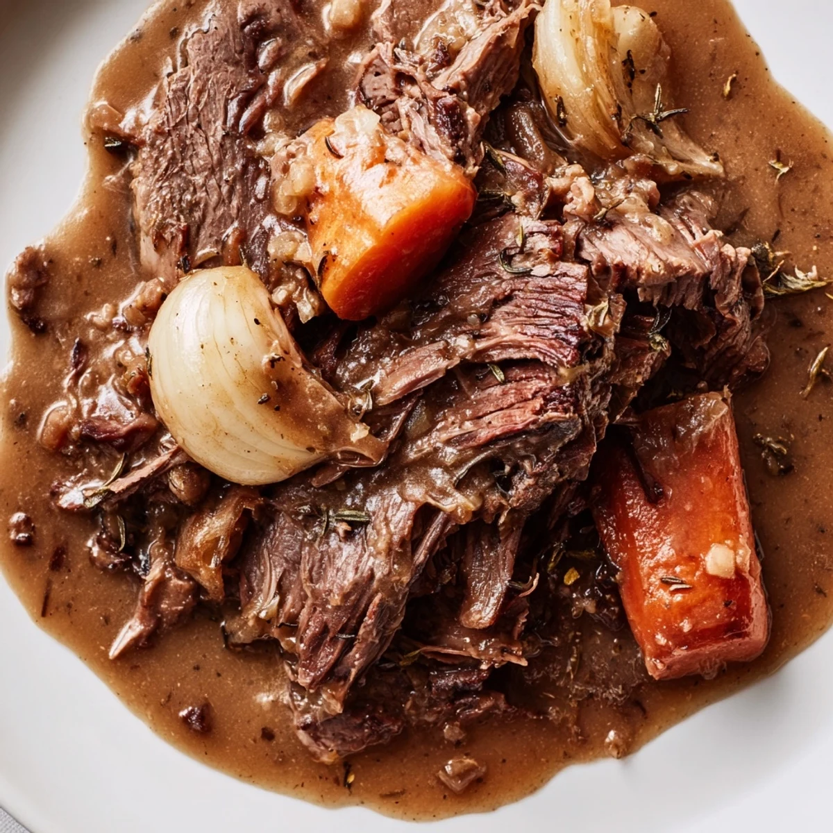 Slow Cooker Roast Beef with Gravy is plated with tender shredded beef, caramelized carrots, and a rich brown sauce spooned over top.