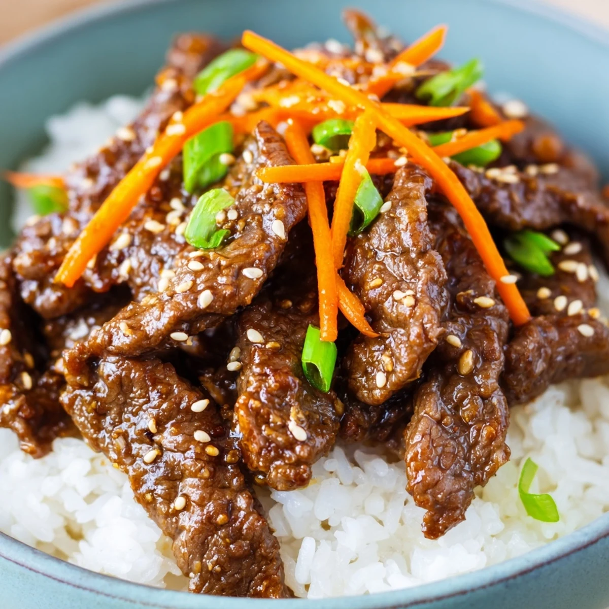 Savory beef strips with onions in a glossy sauce piled high over fluffy white steamed rice in a bowl.