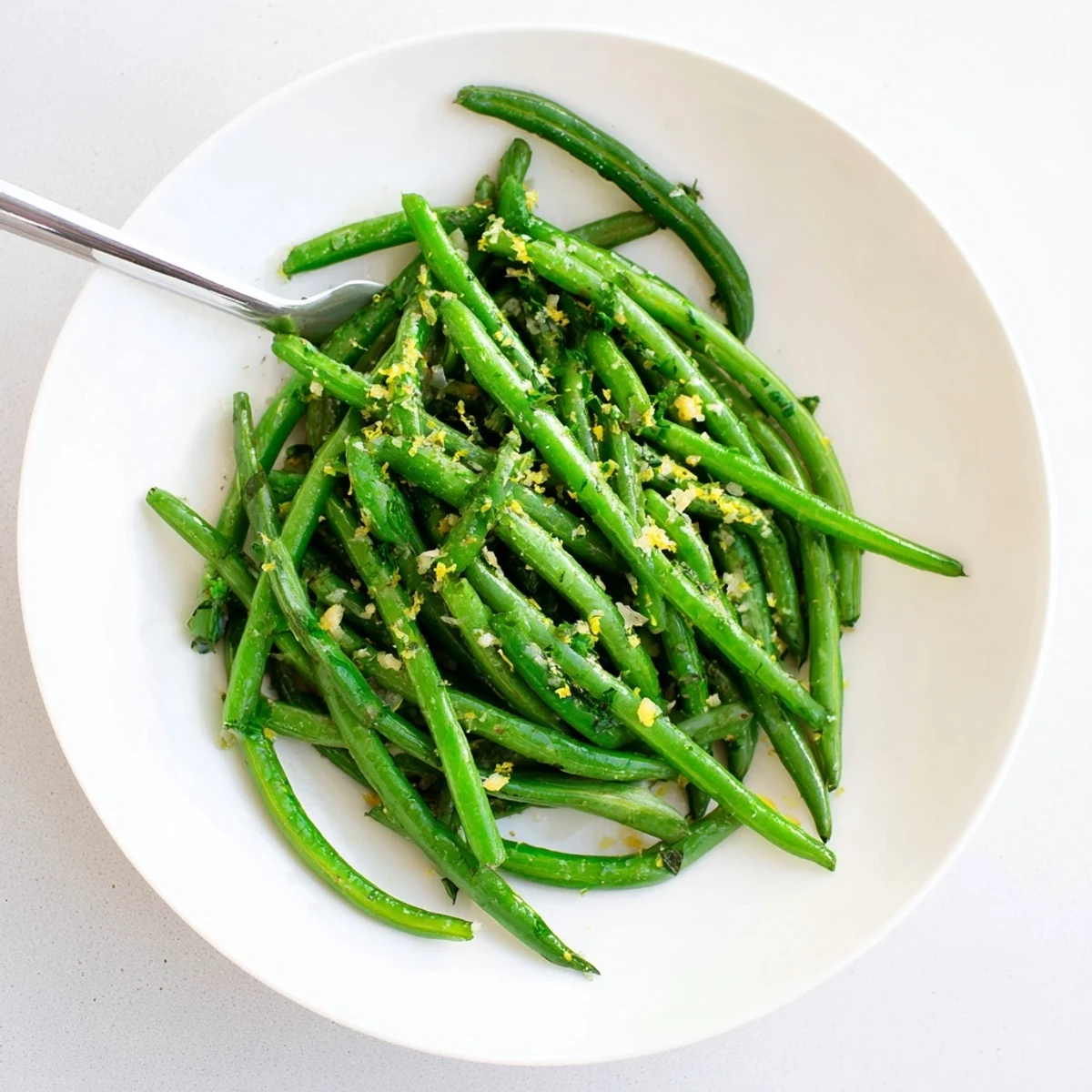 A close-up of crisp-tender sautéed green beans glistening with olive oil, garlic, and bright lemon, ready to serve warm.