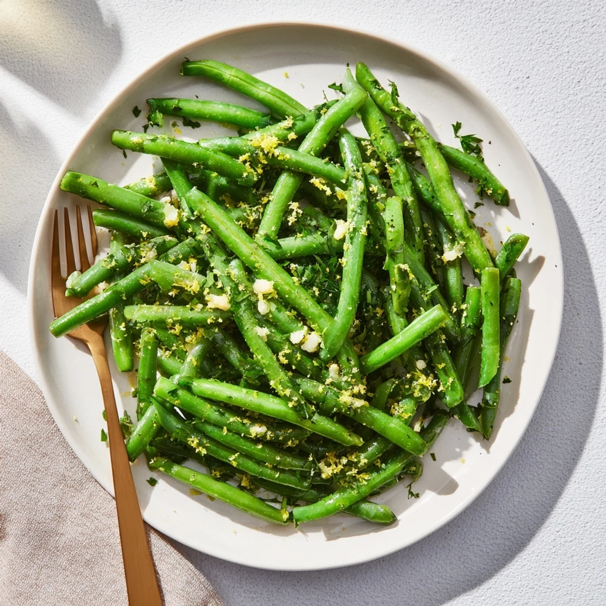 Freshly prepared Lemon Garlic Green Beans on a white platter, garnished with chopped parsley and lemon zest, highlighting the healthy vegan side.