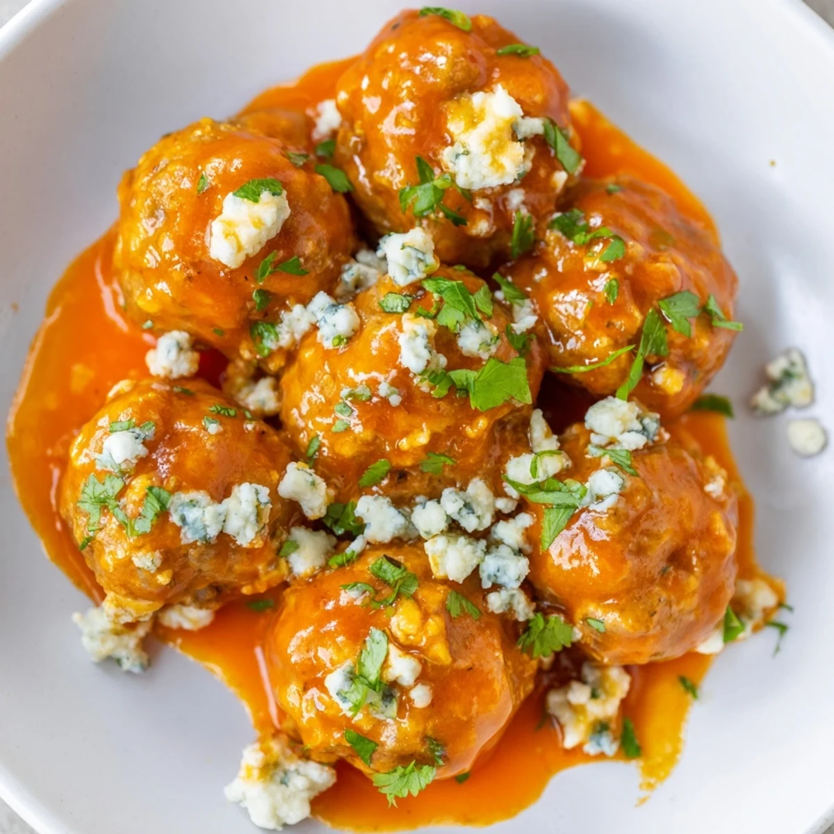 A close-up of Game Day Spicy Buffalo Chicken Meatballs showcases their crispy edges, served with extra blue cheese crumbles and celery sticks for dipping.