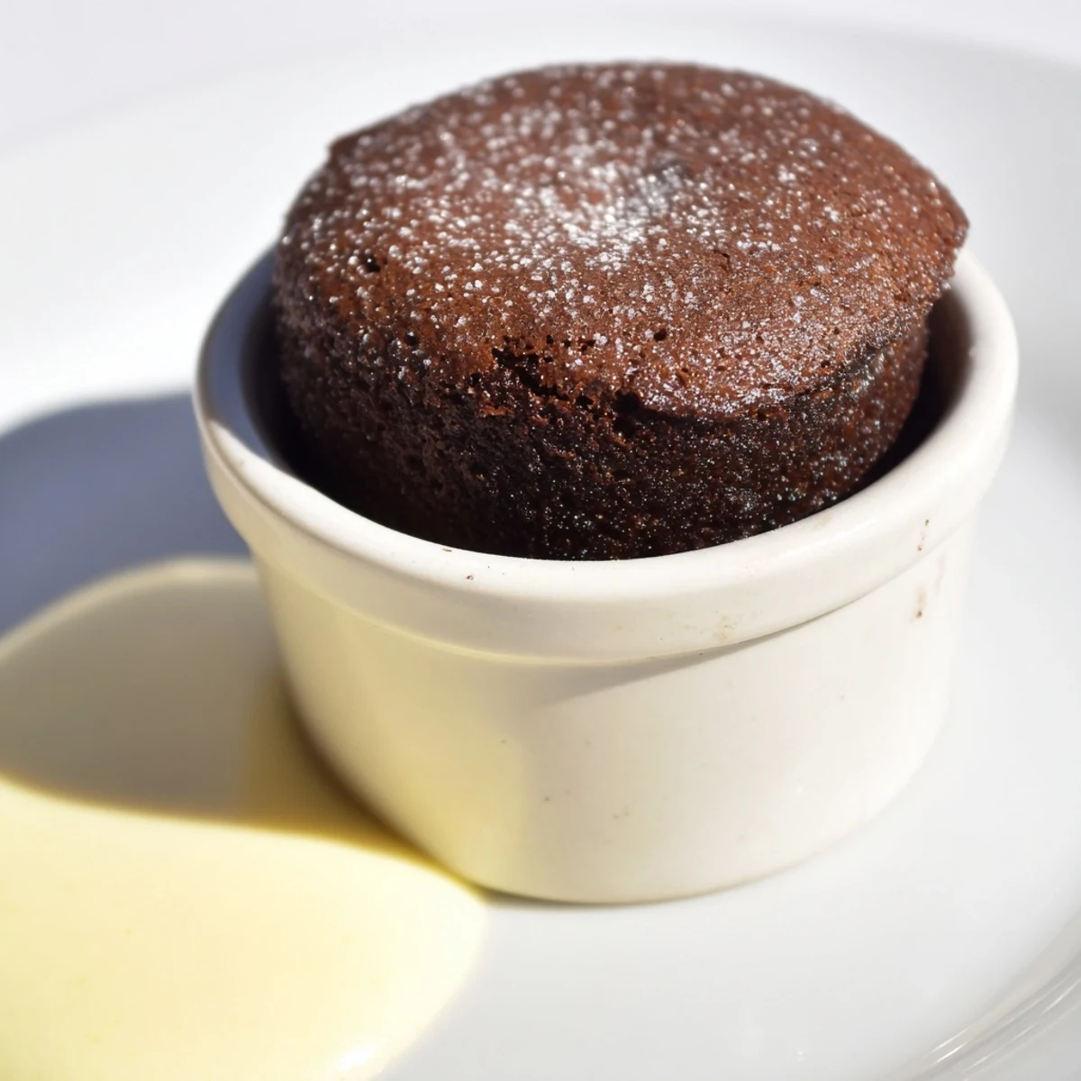 Chocolate Soufflé with Crème Anglaise on a white plate, showing a tender, airy interior and silky custard.