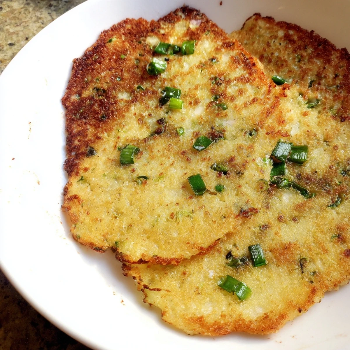 A close-up of crispy Irish Boxty Potato Pancakes garnished with fresh green scallions.