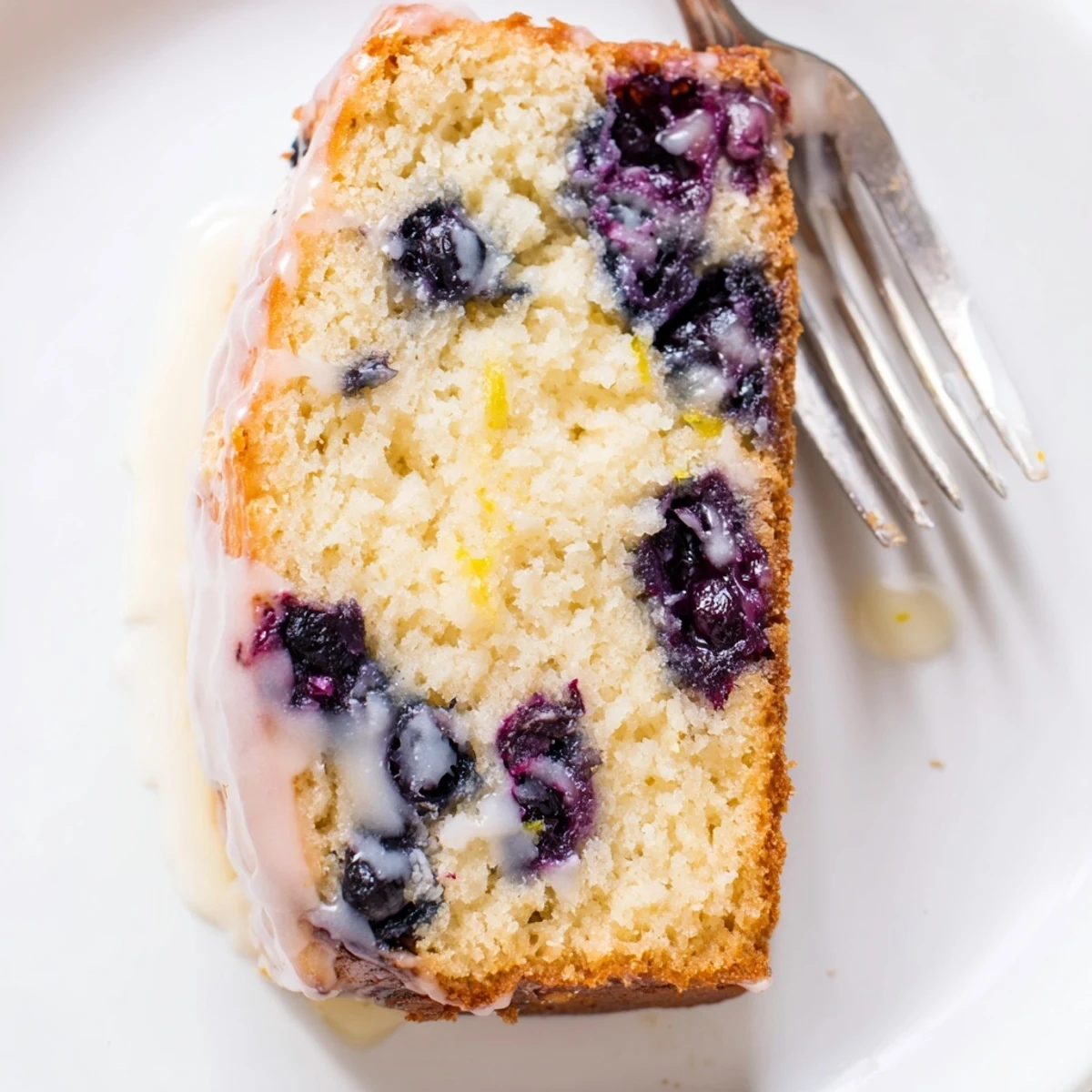 Golden-brown Lemon Blueberry Yogurt Loaf Cake with a glossy lemon glaze, studded with fresh blueberries and sliced on a wooden board.