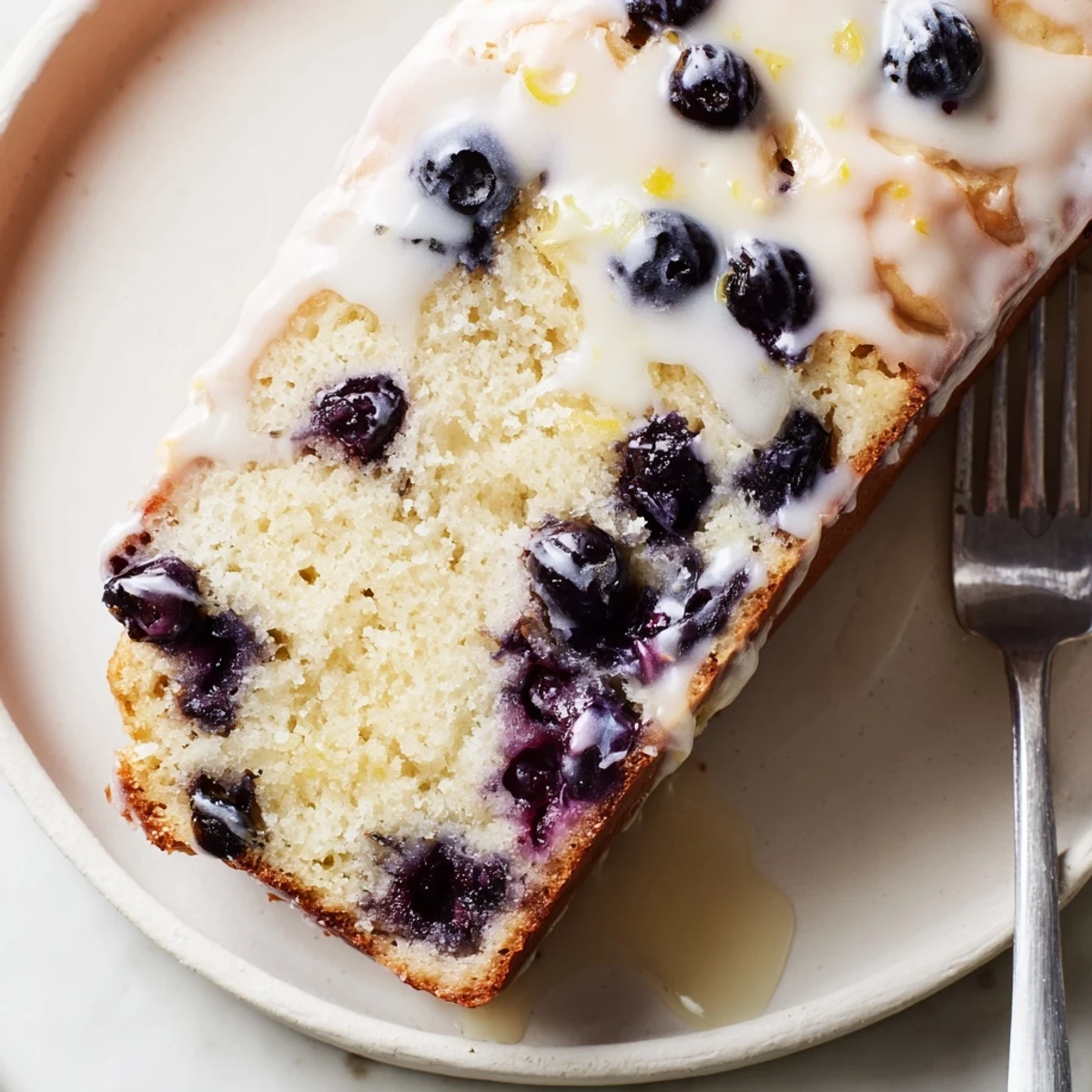 Freshly glazed Lemon Blueberry Yogurt Loaf Cake on a marble countertop, ready to be served for breakfast or with afternoon tea.