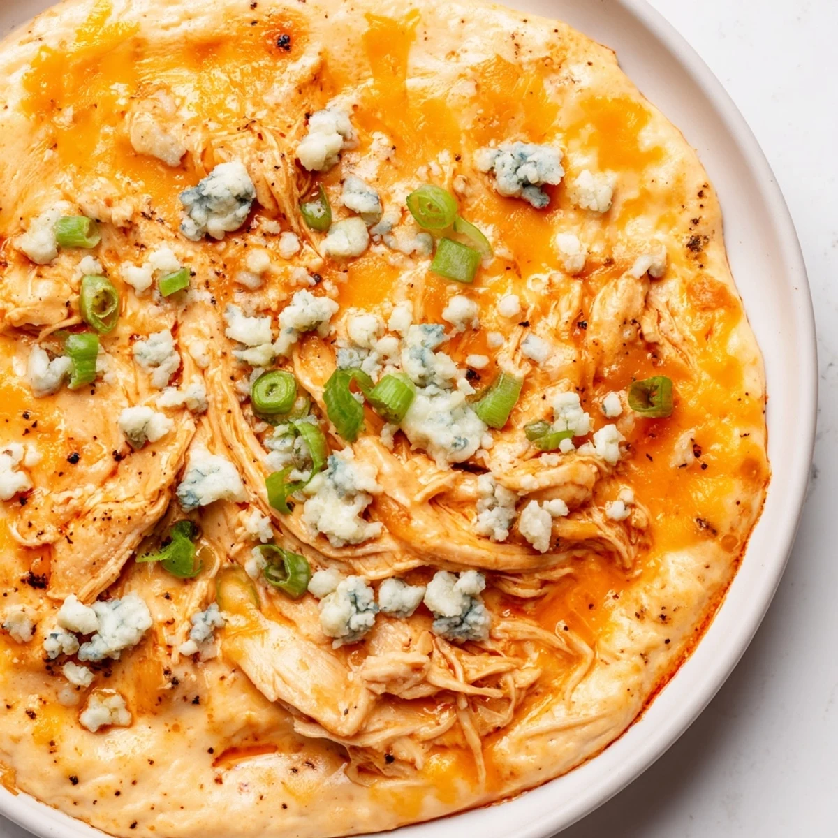 Spicy Keto Buffalo Chicken Dip bubbling from the oven, golden top, with ranch drizzle and sliced green onions for garnish.