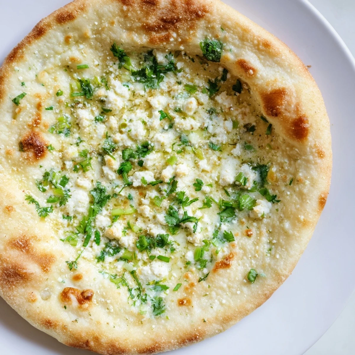 A close-up of freshly cooked Cottage Cheese Garlic Naan, speckled with minced garlic and cilantro, served warm beside a bowl of curry.  