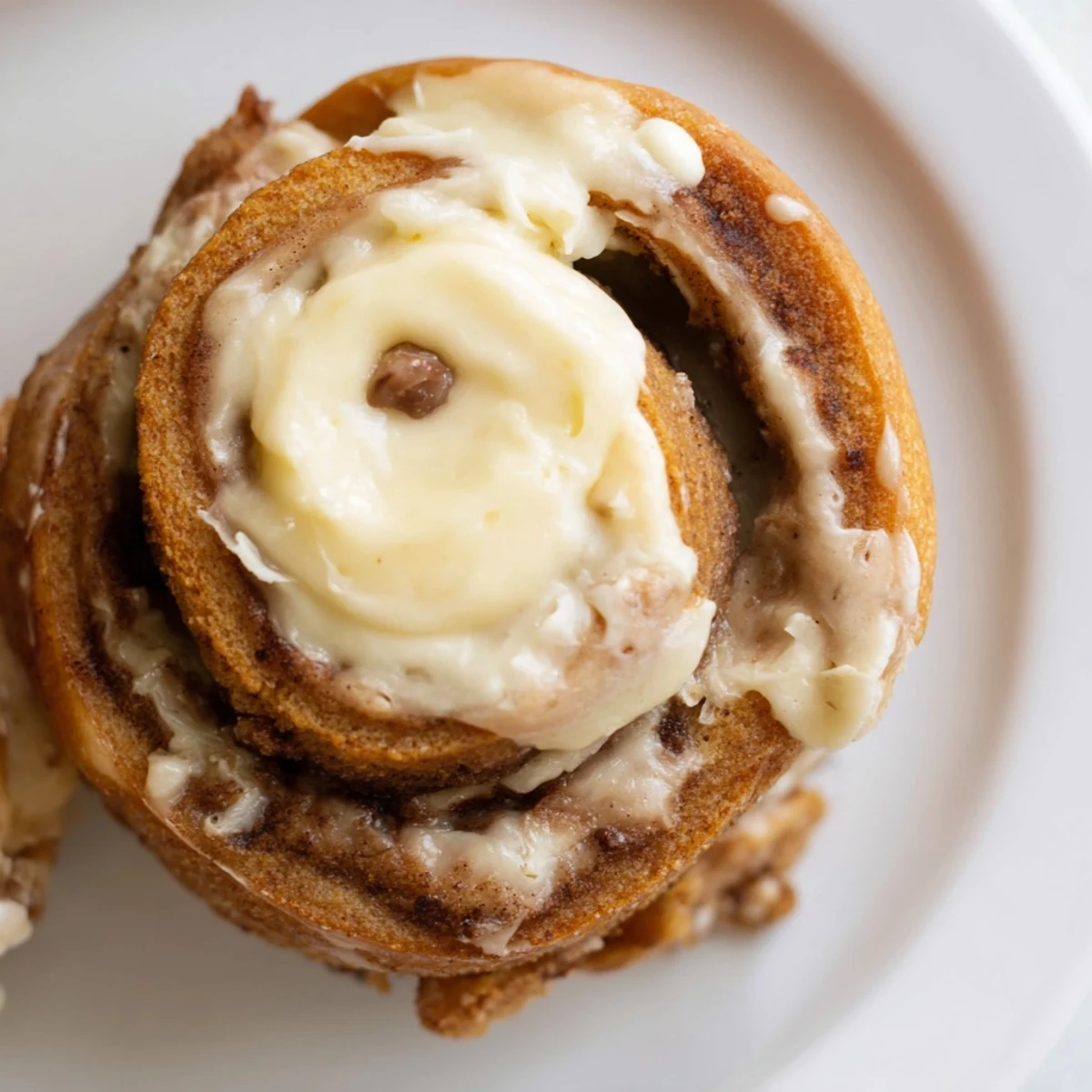Freshly glazed Keto Cinnamon Buns served on a white plate with a cup of coffee nearby.