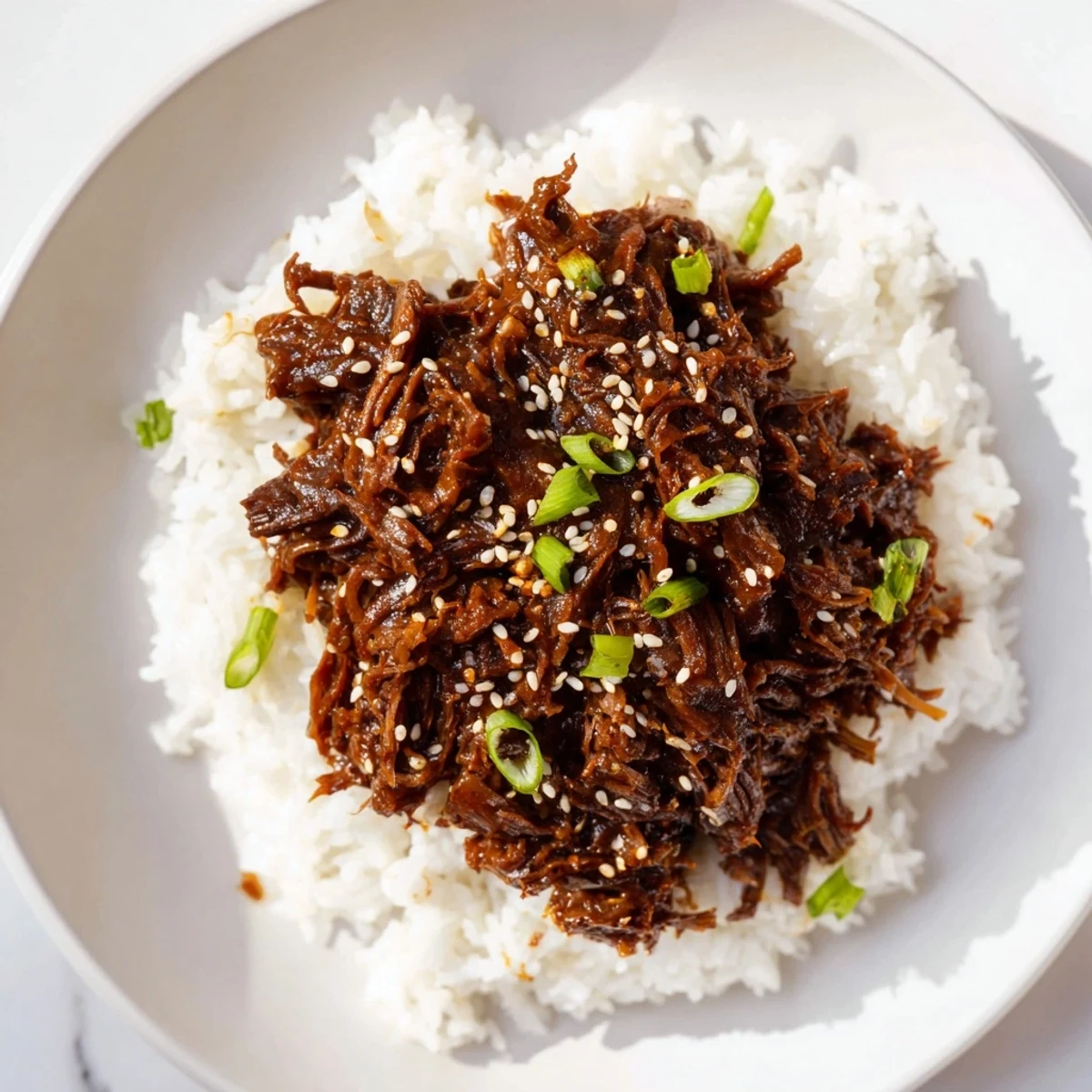 Tender chunks of Slow Cooker Korean Beef simmered in a sticky, sweet sauce, served over fluffy white rice with sesame garnish.