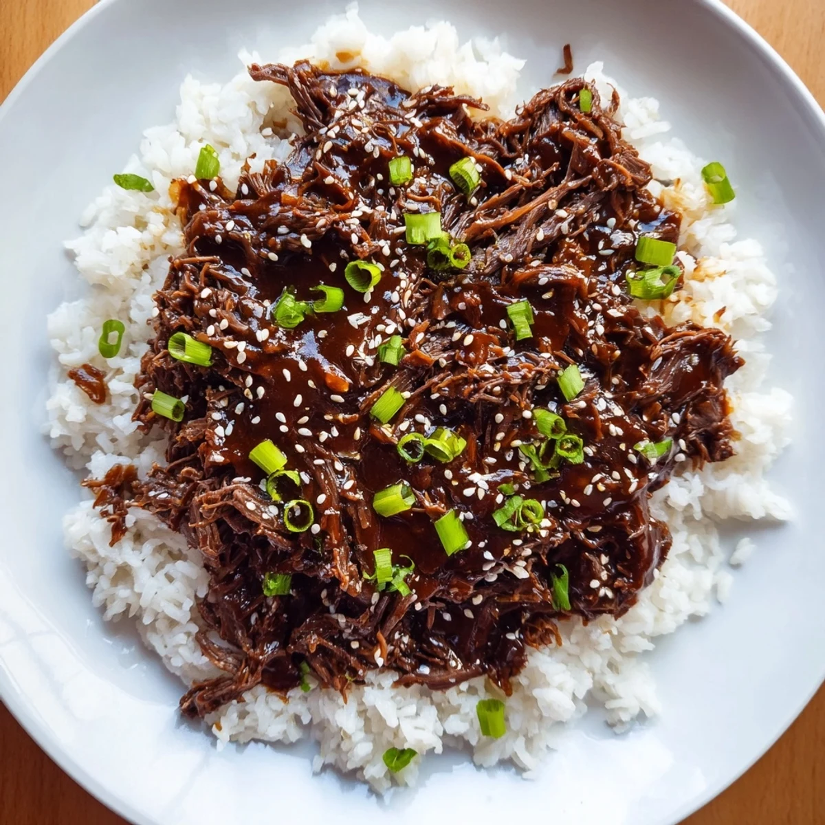 A bowl of Slow Cooker Korean Beef, glistening with sauce alongside steamed rice and vibrant pickled vegetables for a complete meal.