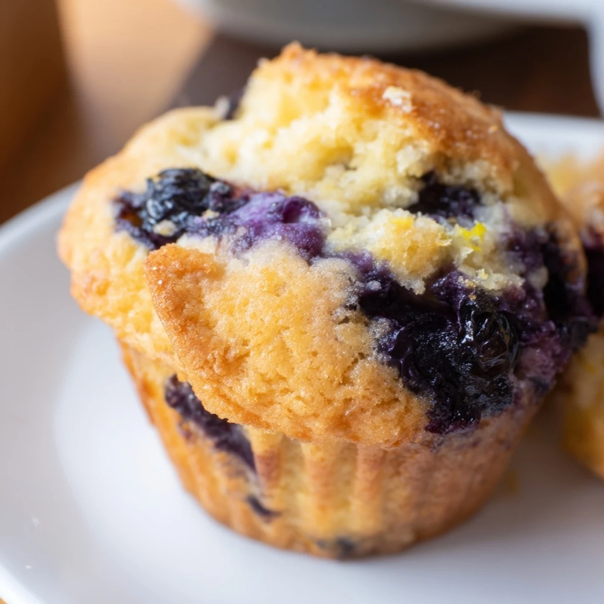 A single warm Sourdough Blueberry Muffin rests beside a cup of coffee, highlighting the breakfast-ready texture.
