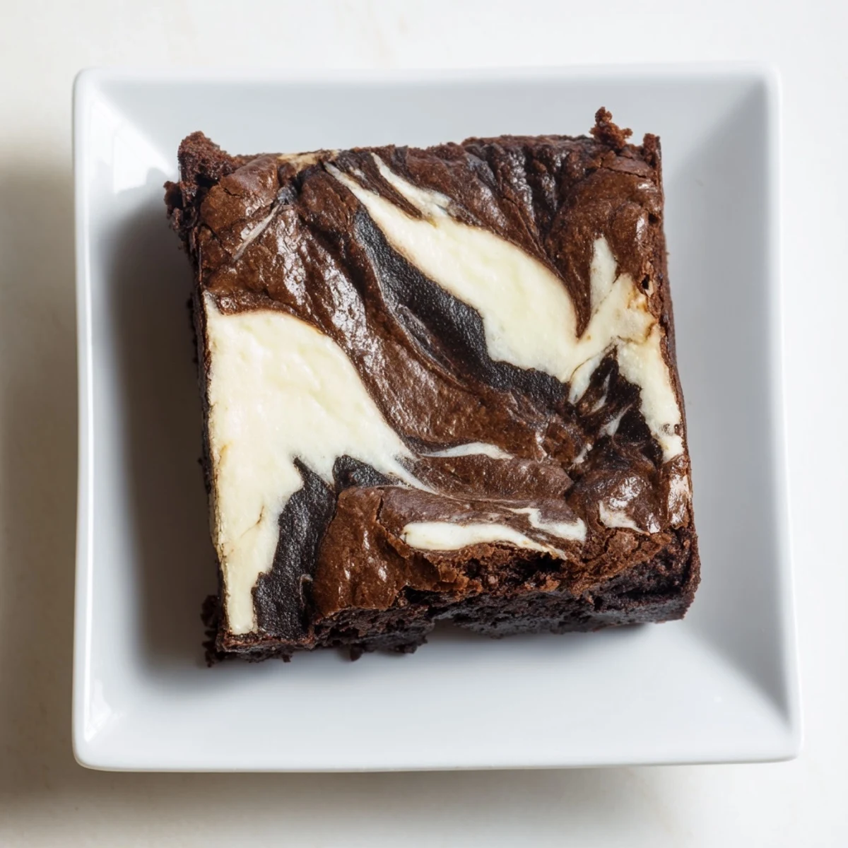 Decadent Cottage Cheese Brownies on a white plate, with a bite taken out revealing a fudgy interior and creamy cottage cheese swirl.