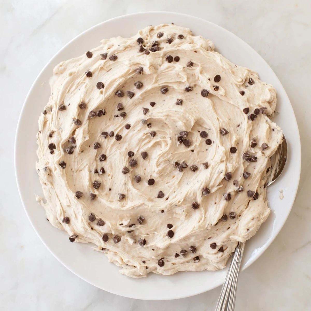 Close-up of Cookie Dough Frosting on cupcakes, with a spoon ready for tasting, highlighting its creamy, cookie dough texture.