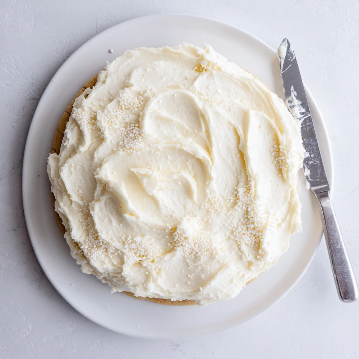 Two homemade sugar cookies topped with generous swirls of creamy Easy Sugar Cookie Frosting on a white plate ready to serve.