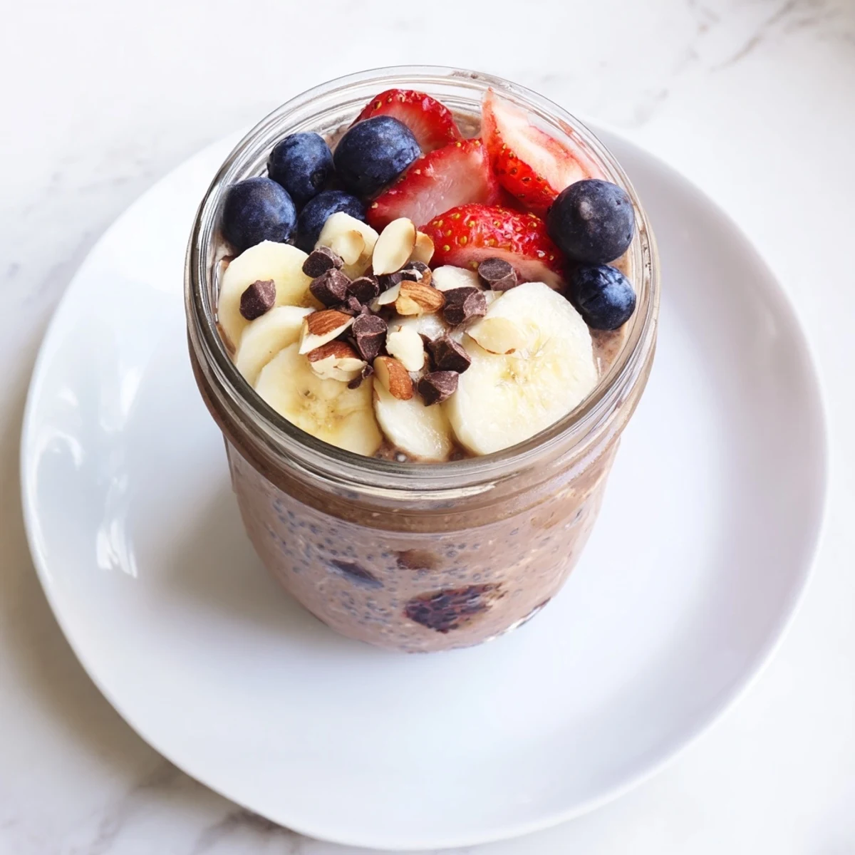 Creamy Ultimate Healthy Chocolate Overnight Oats in a glass jar, topped with fresh berries and sliced banana.