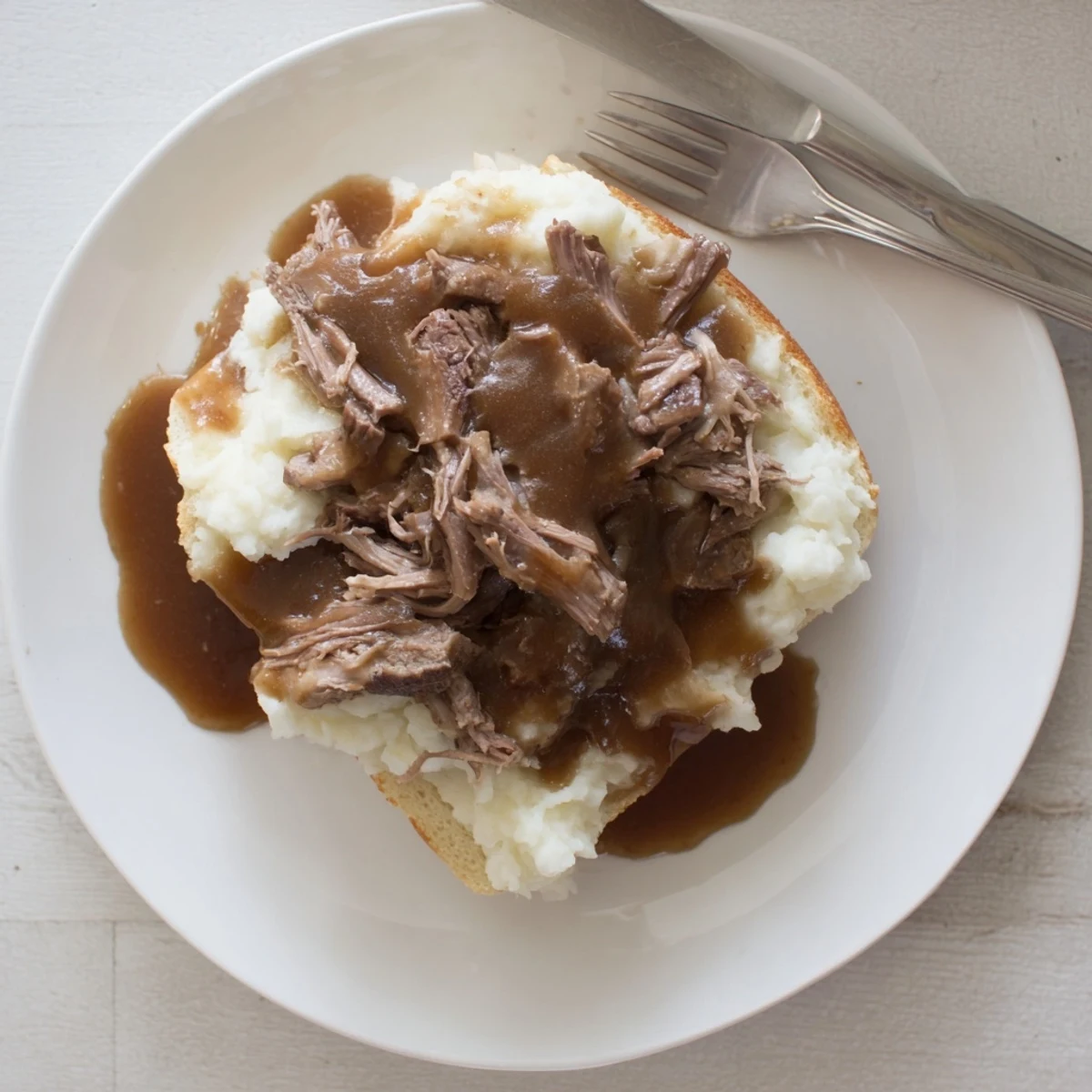 Shredded Slow Cooker Beef Manhattan piled on bread with creamy mashed potatoes and rich brown gravy for a hearty meal.