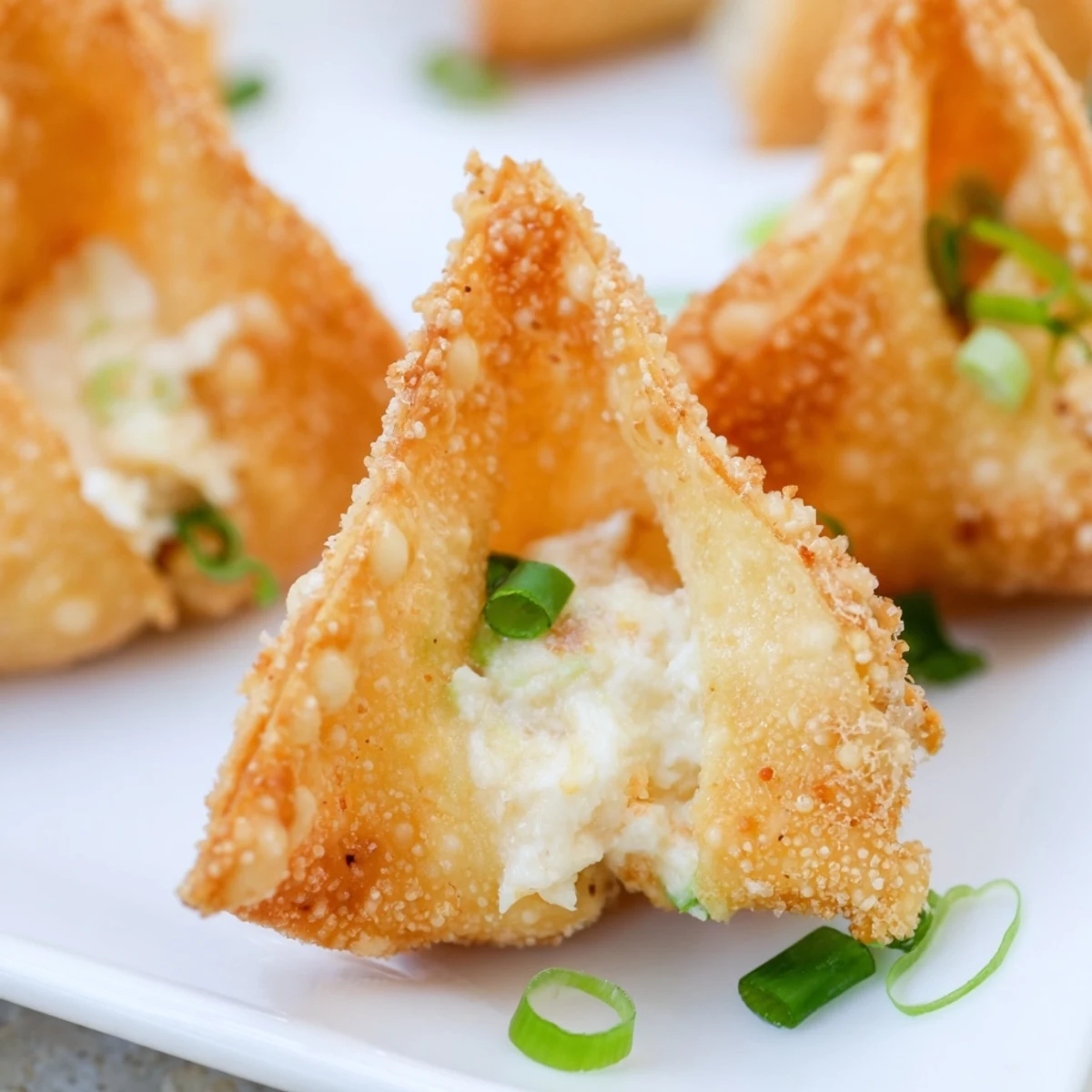 Golden crispy Crispy Crab Rangoon Bombs with Creamy Filling rest on a plate beside a small bowl of sweet chili dipping sauce.