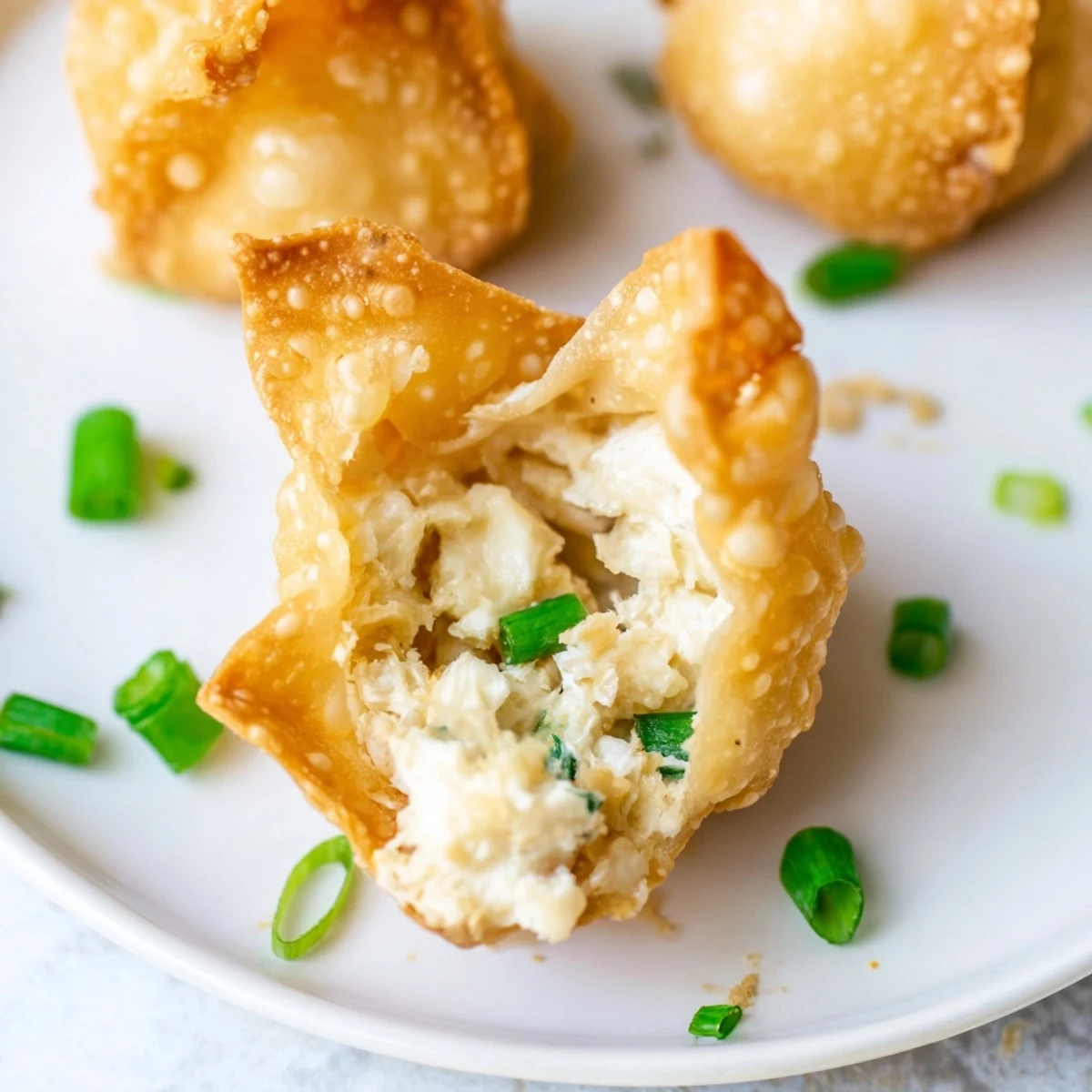 Freshly fried Crispy Crab Rangoon Bombs with Creamy Filling display their golden-brown wonton wrappers and are topped with green chives.