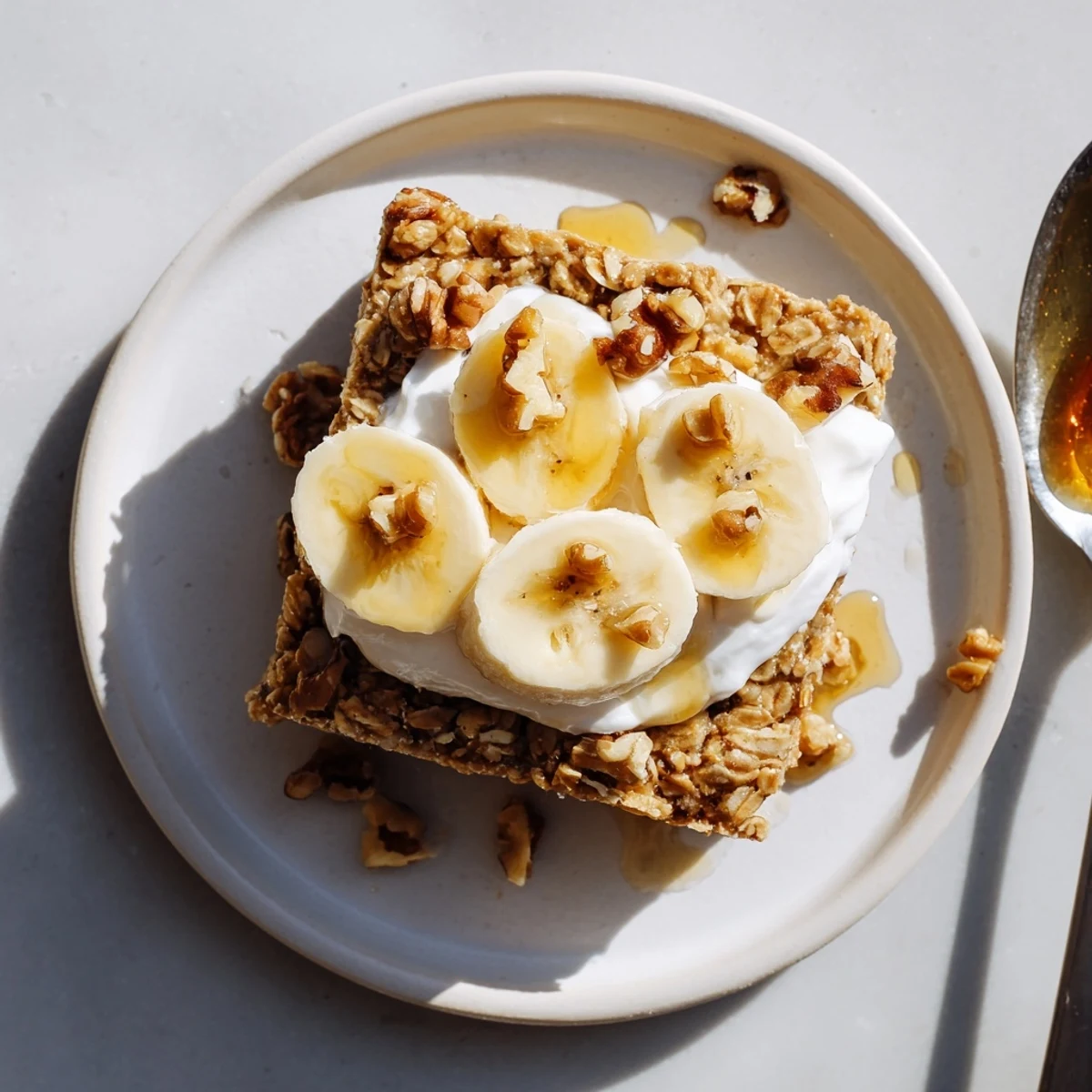 Golden-brown slices of Banana Baked Oatmeal with Greek Yogurt topped with fresh banana rounds and a honey drizzle.
