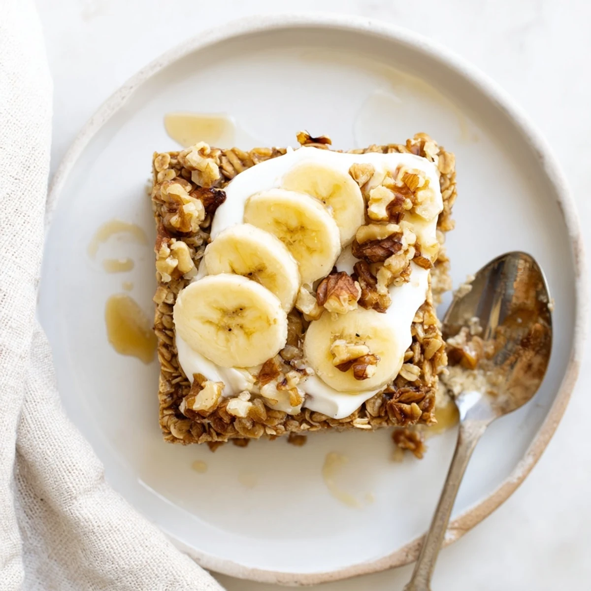 A cozy close-up of Banana Baked Oatmeal with Greek Yogurt, steaming on a plate beside a warm mug of coffee.