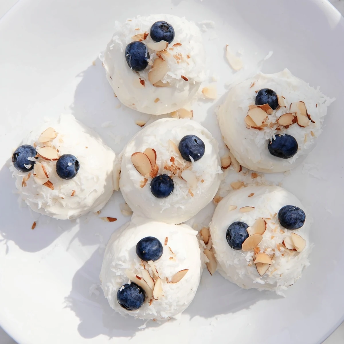 Frozen blueberry Greek yogurt bites garnished with chopped pistachios and shredded coconut on a white plate