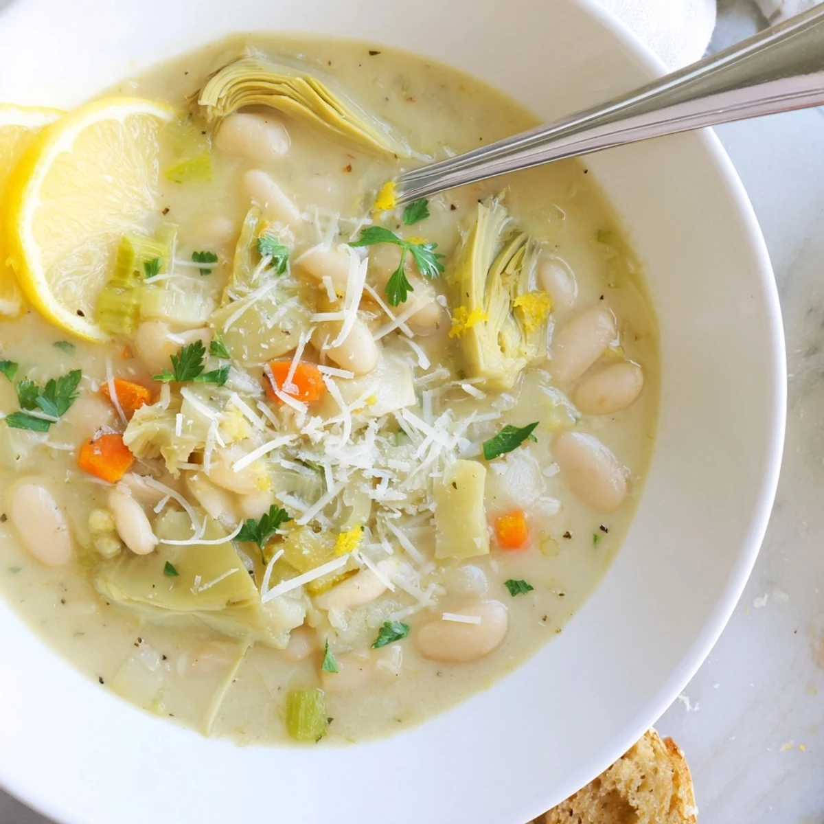 Rustic white bowl of zesty Tuscan artichoke soup served with lemon wedges and parmesan