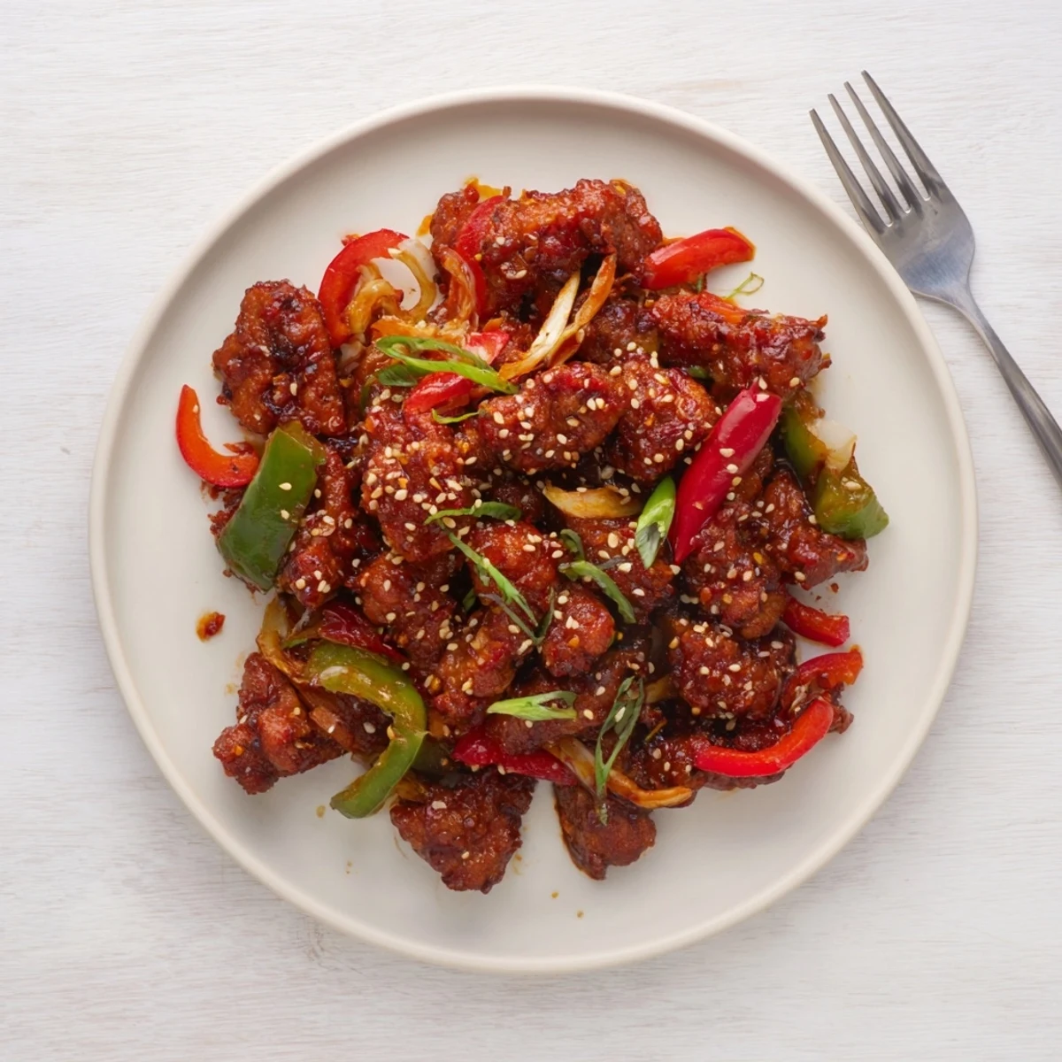 Homemade crispy chilli beef with crispy fried beef strips coated in glossy sweet spicy sauce alongside spring onions