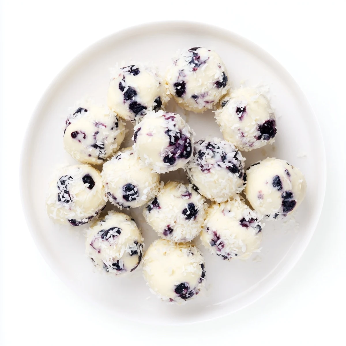 Hand holding a blueberry cheesecake protein bite showcasing the soft interior and shredded coconut coating