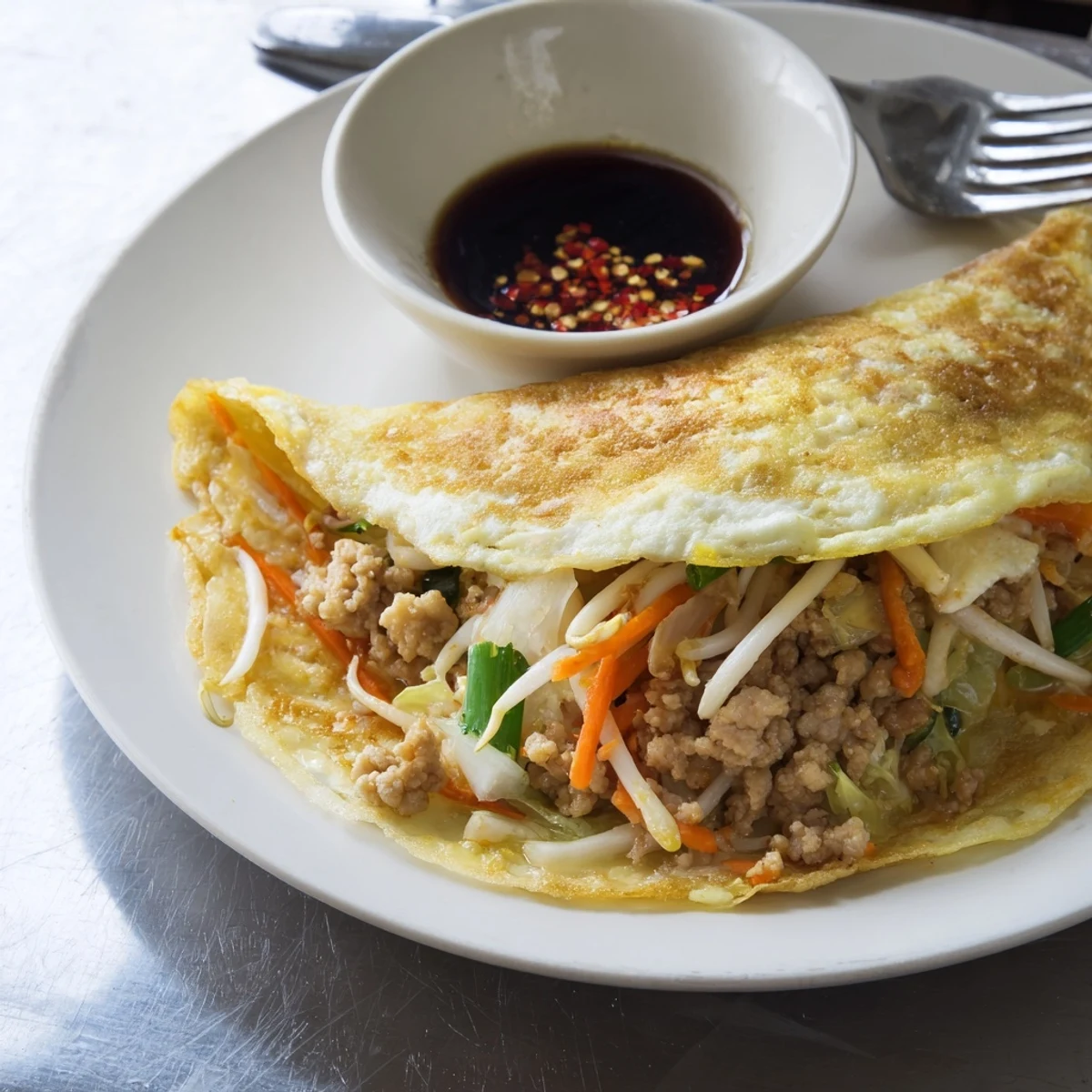 Close up of golden brown stuffed breakfast pancake drizzled with dipping sauce and garnished with fresh scallions