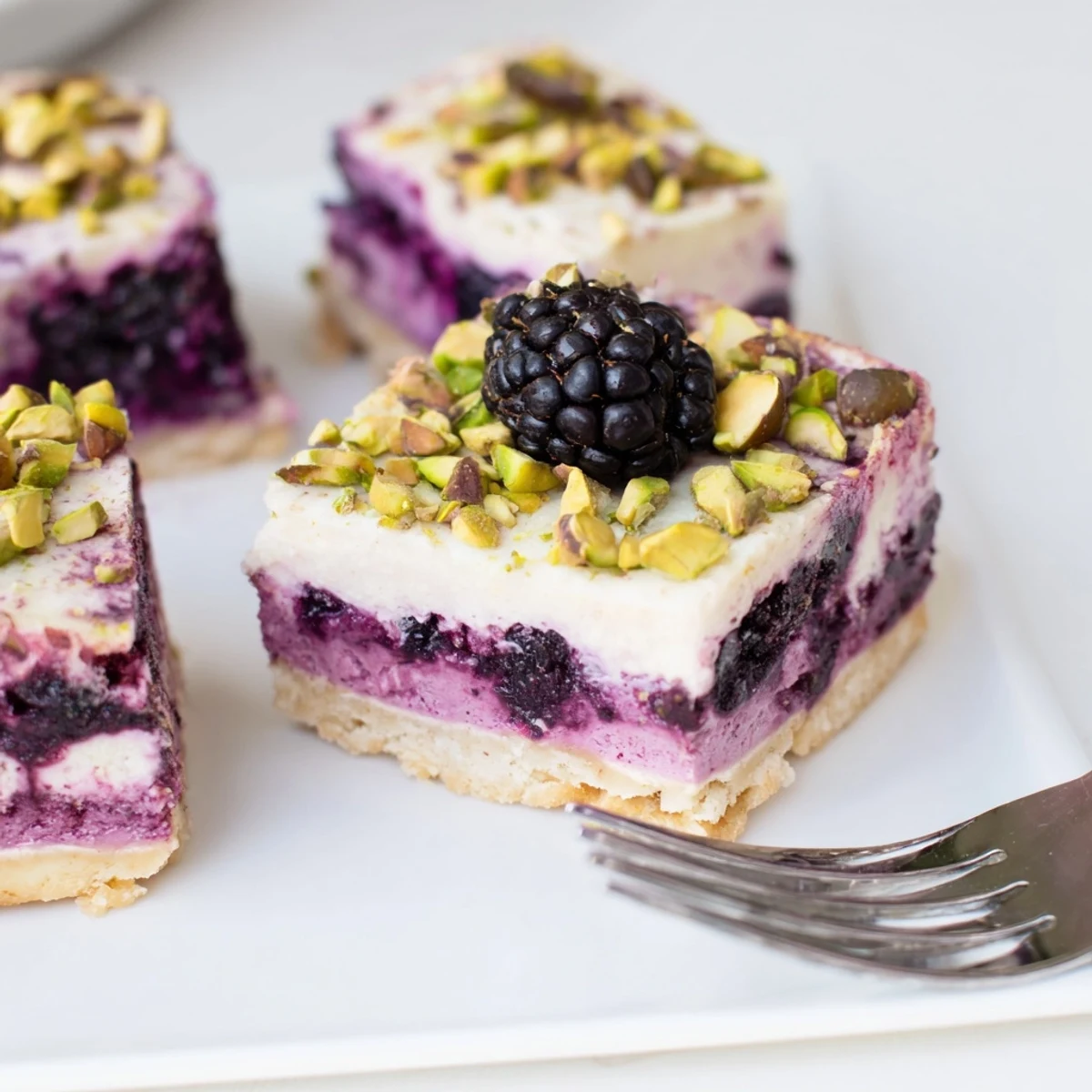 Golden Blackberry Pistachio Dream Bars layered with purple fruit swirls and creamy white cheesecake topping on a green-speckled crust