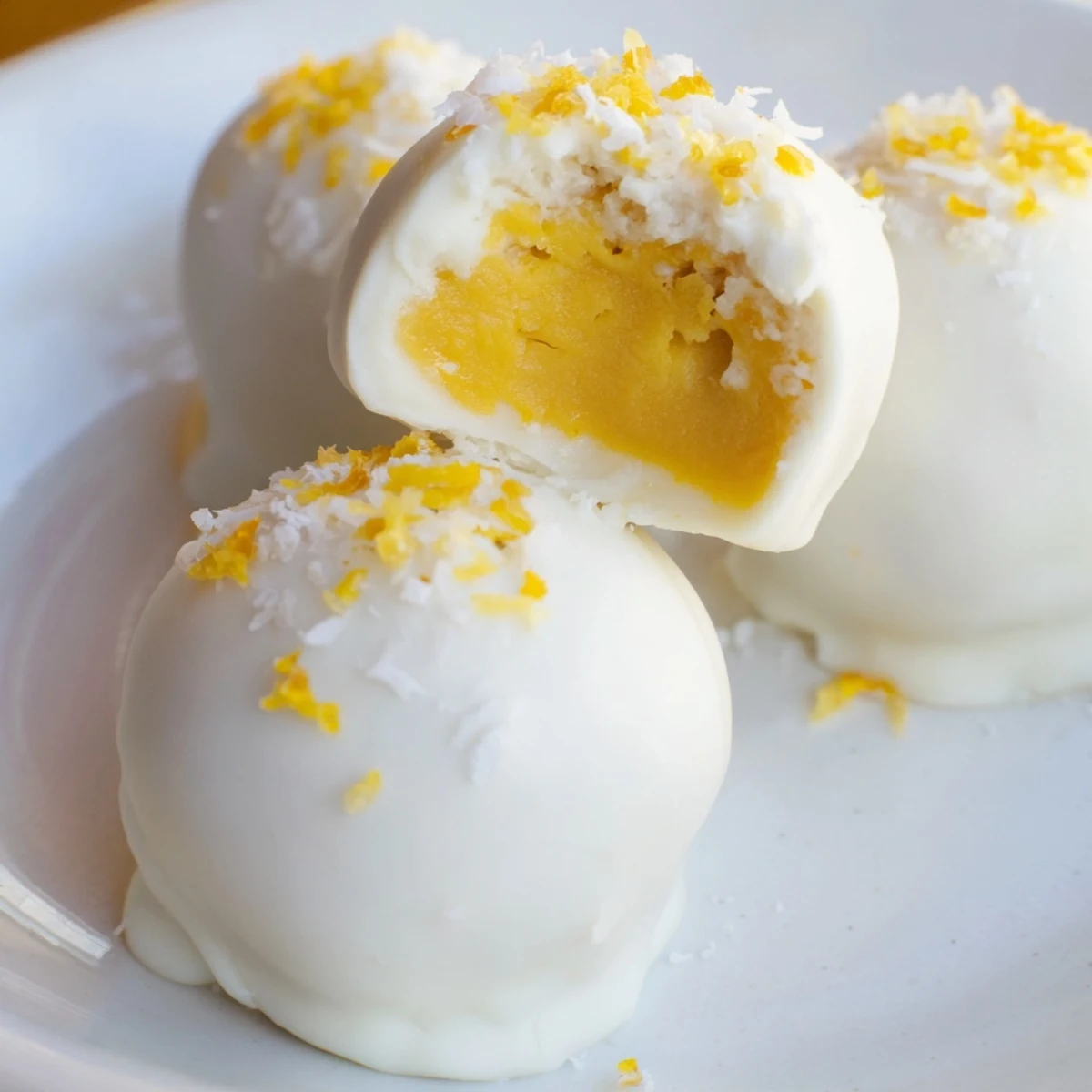 Creamy mango truffles coated in white chocolate with dried mango garnish on a white plate