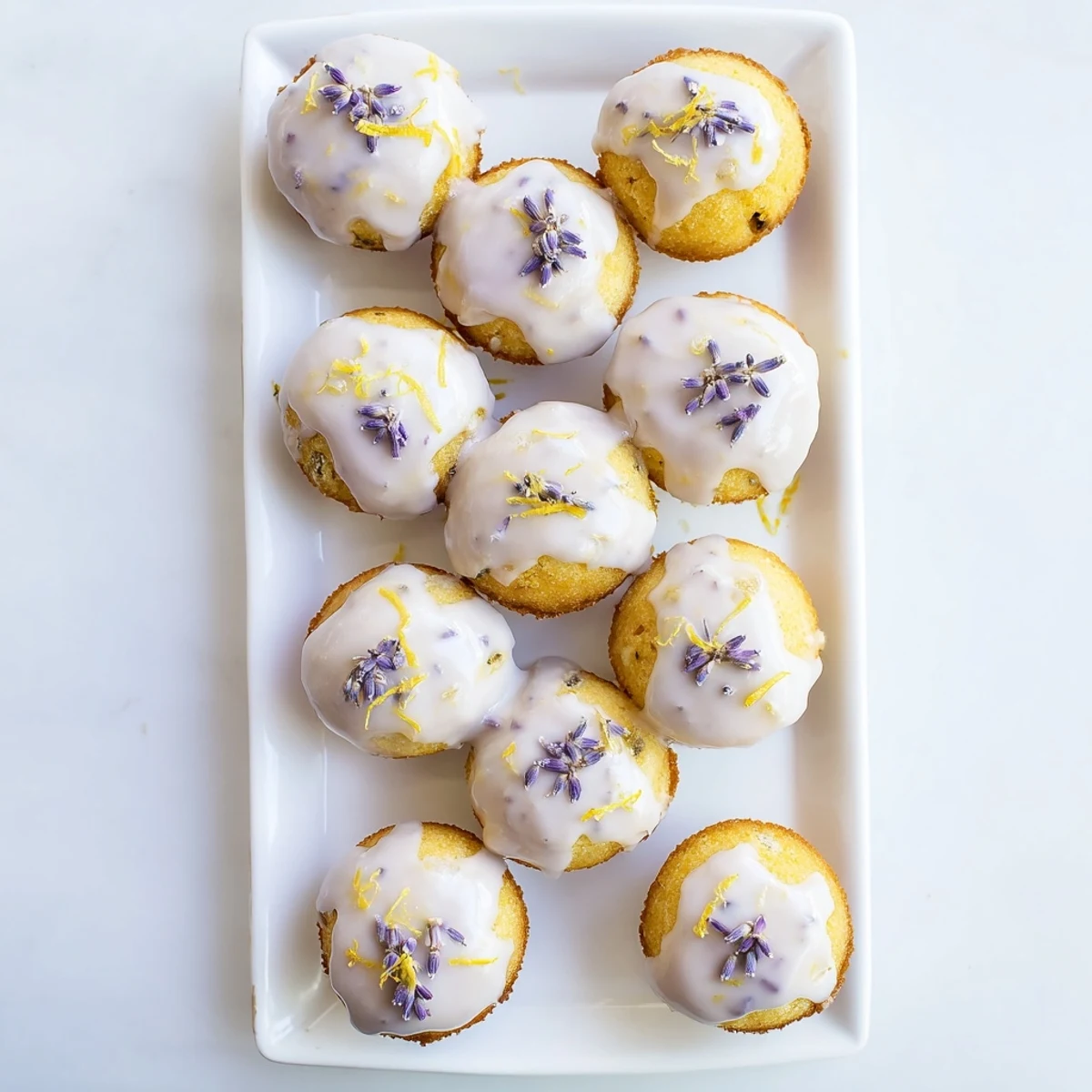 Golden mini lemon cakes drizzled with purple lavender glaze on a white serving plate