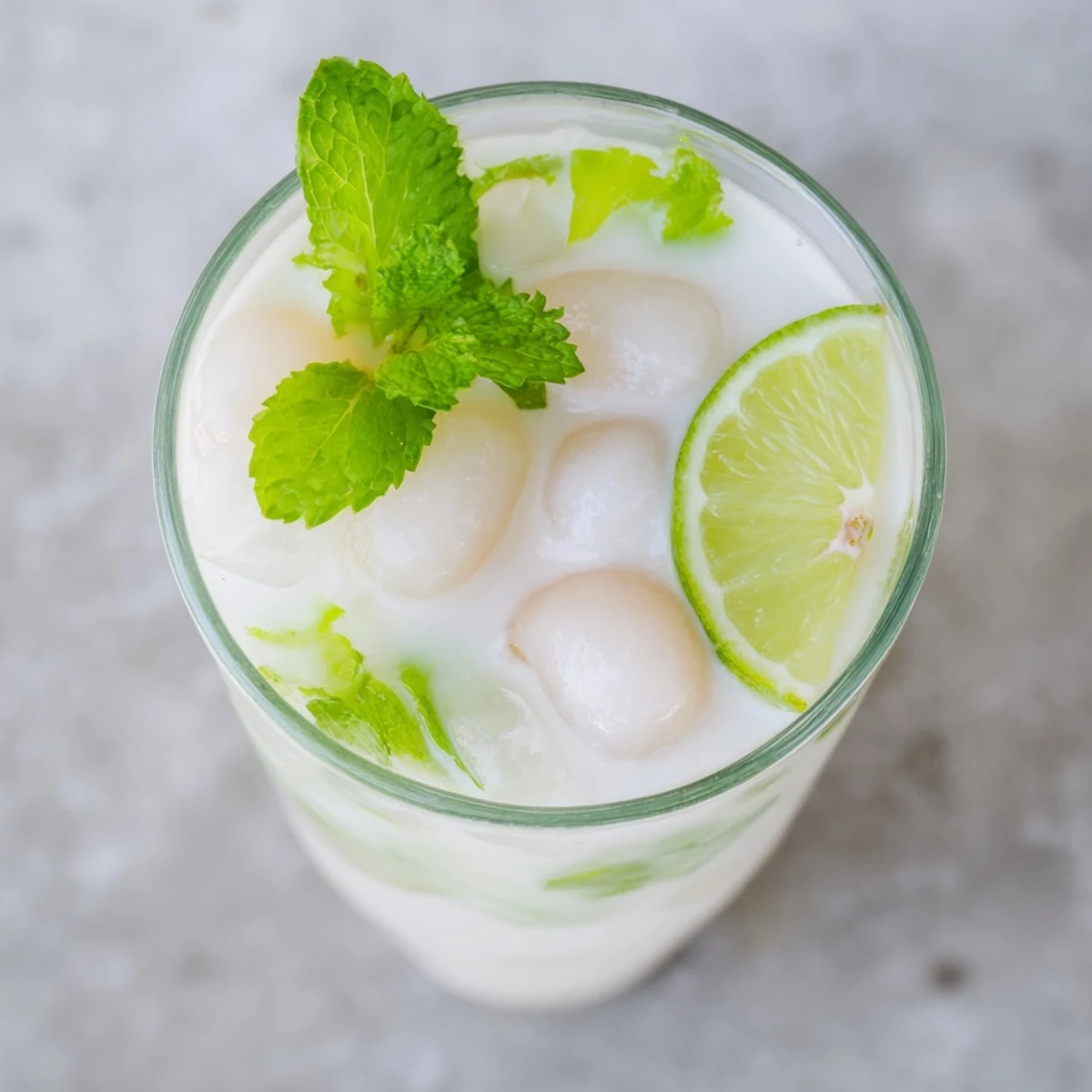 Creamy Coconut Lychee Iced Drink served in tall glasses with fresh mint leaves and lime garnish