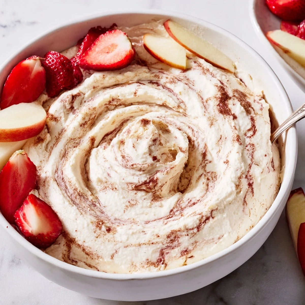 Creamy Greek yogurt cinnamon roll dip swirled with cinnamon and served with fresh sliced apples and strawberries on a wooden platter