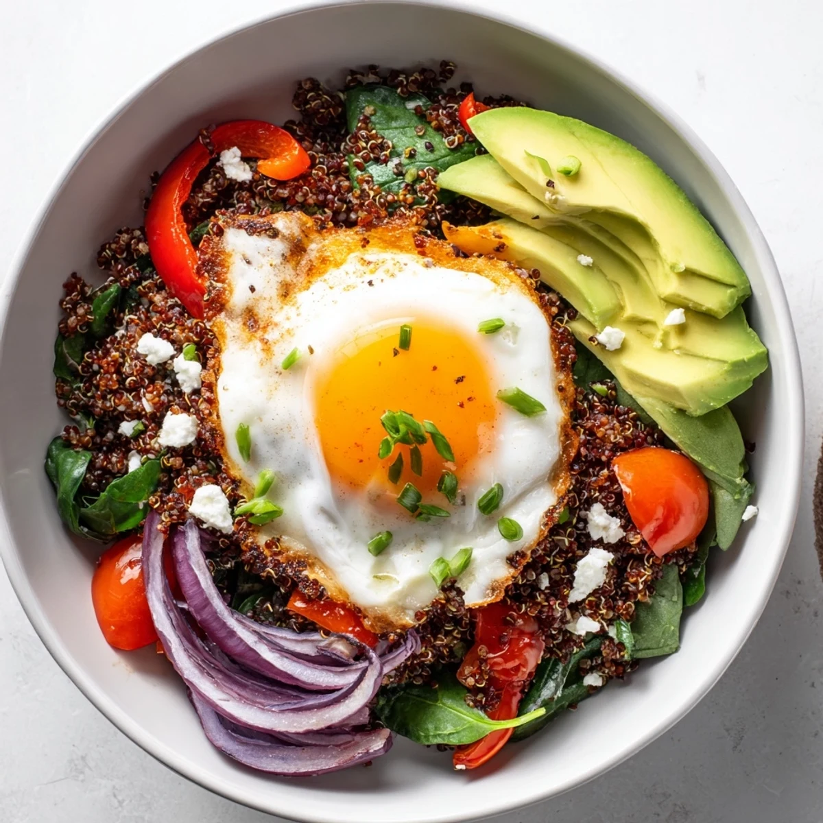Golden fried egg atop fluffy quinoa breakfast bowl with colorful sautéed vegetables and fresh herbs