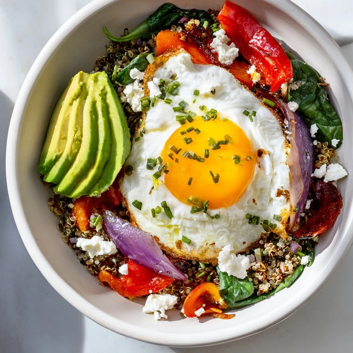 Hearty quinoa breakfast bowl in white serving dish topped with runny egg, diced peppers, and chives