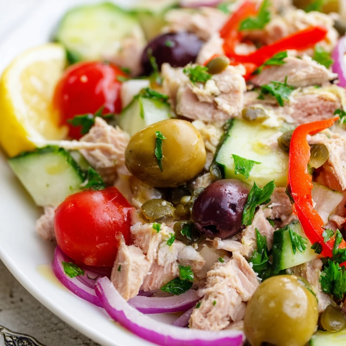 Mediterranean tuna salad in a white bowl with cherry tomatoes, olives, and fresh herbs