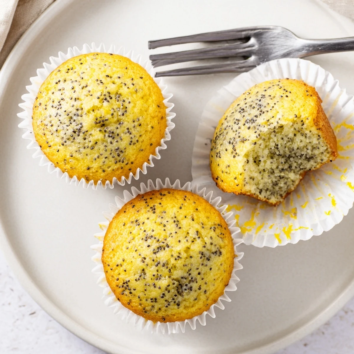 Moist lemon poppy seed muffins speckled with zest arranged on a rustic ceramic plate