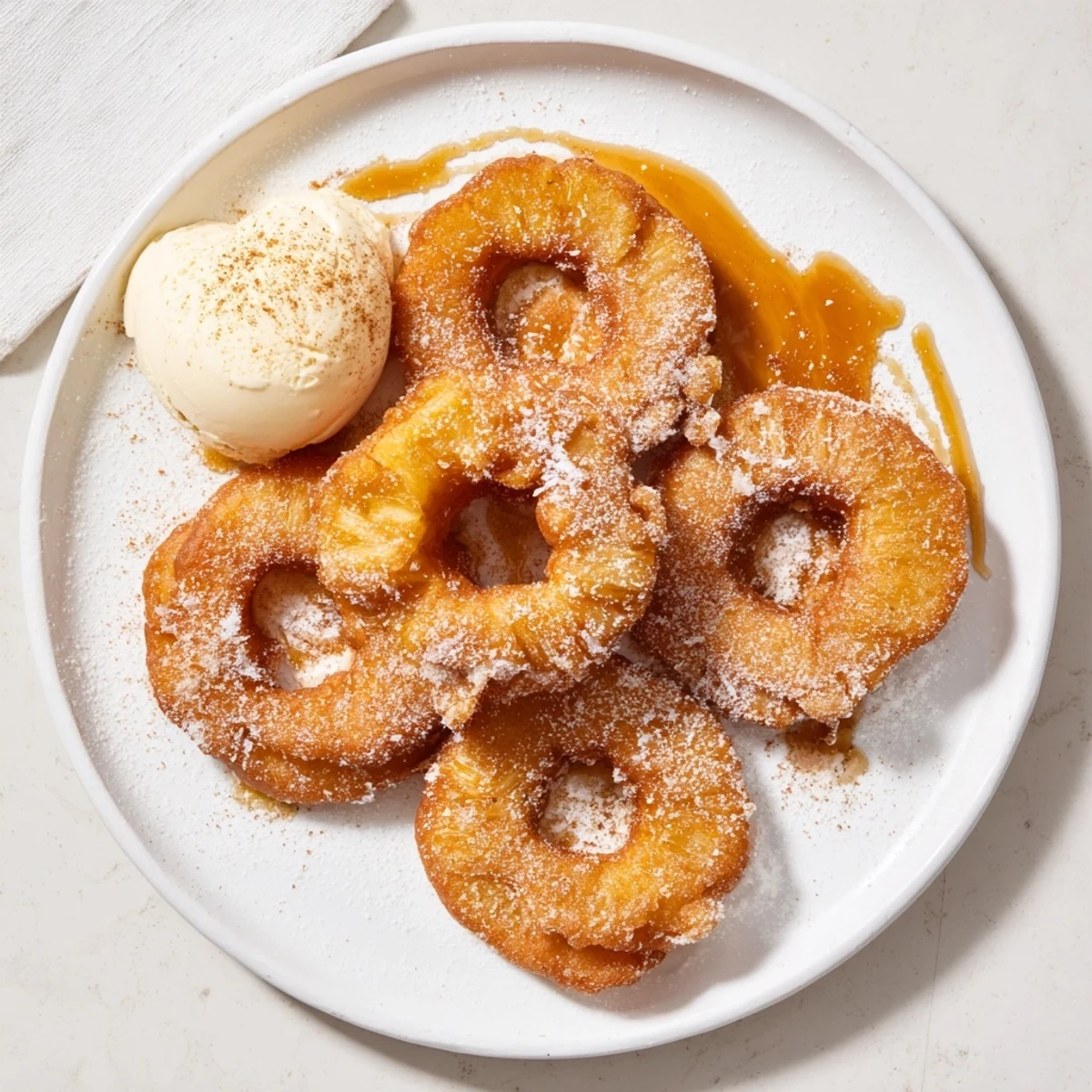 Battered fried pineapple rings drizzled with caramel sauce beside vanilla ice cream