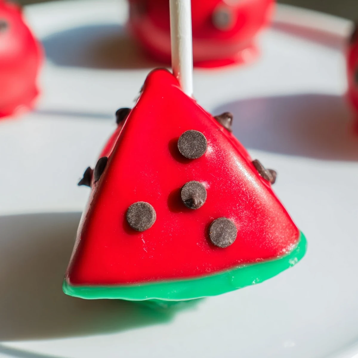 Watermelon cake pops on lollipop sticks displaying pink centers with green rinds and chocolate chip seeds
