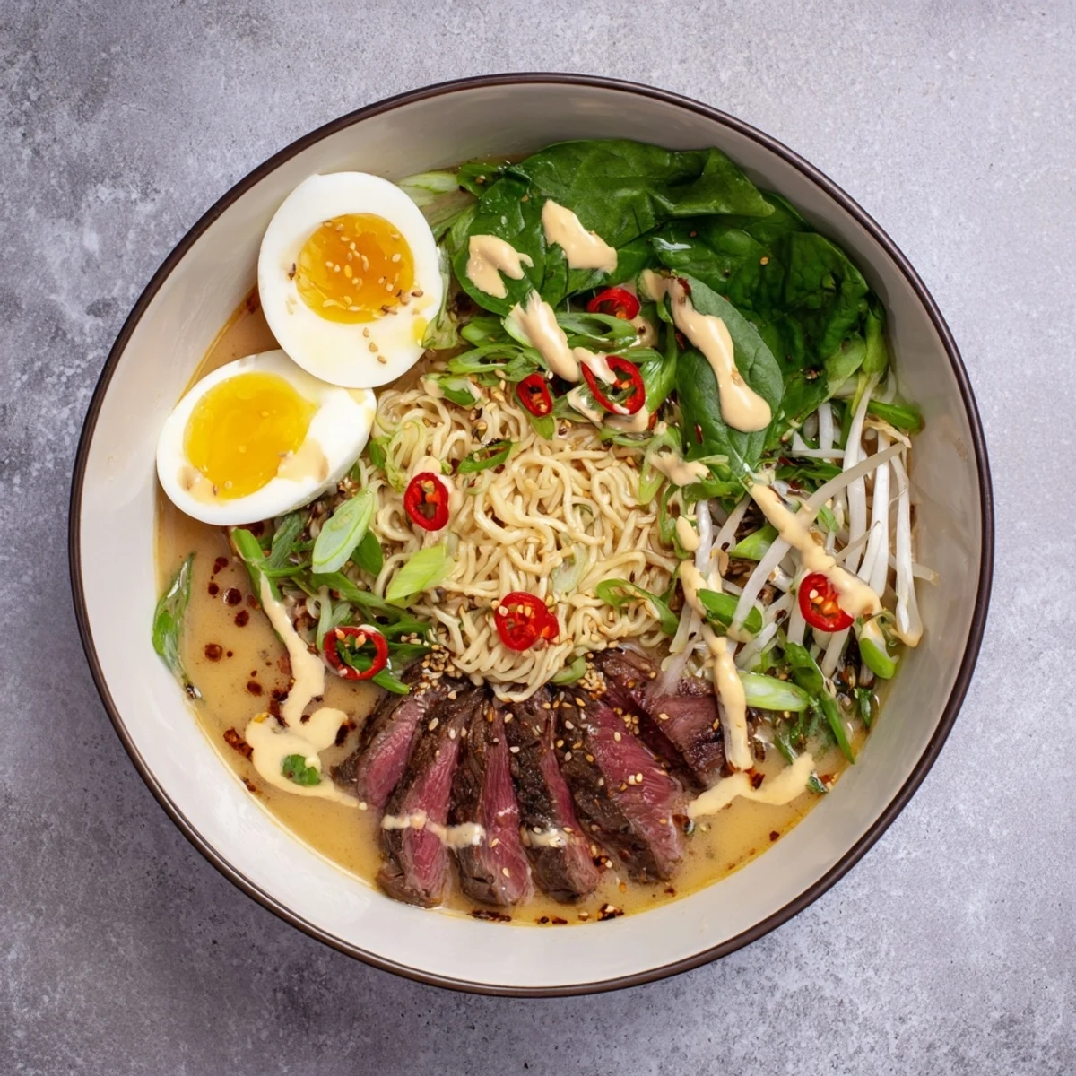 Steaming bowl of spicy beef ramen with creamy garlic sauce drizzled over tender noodles and toppings