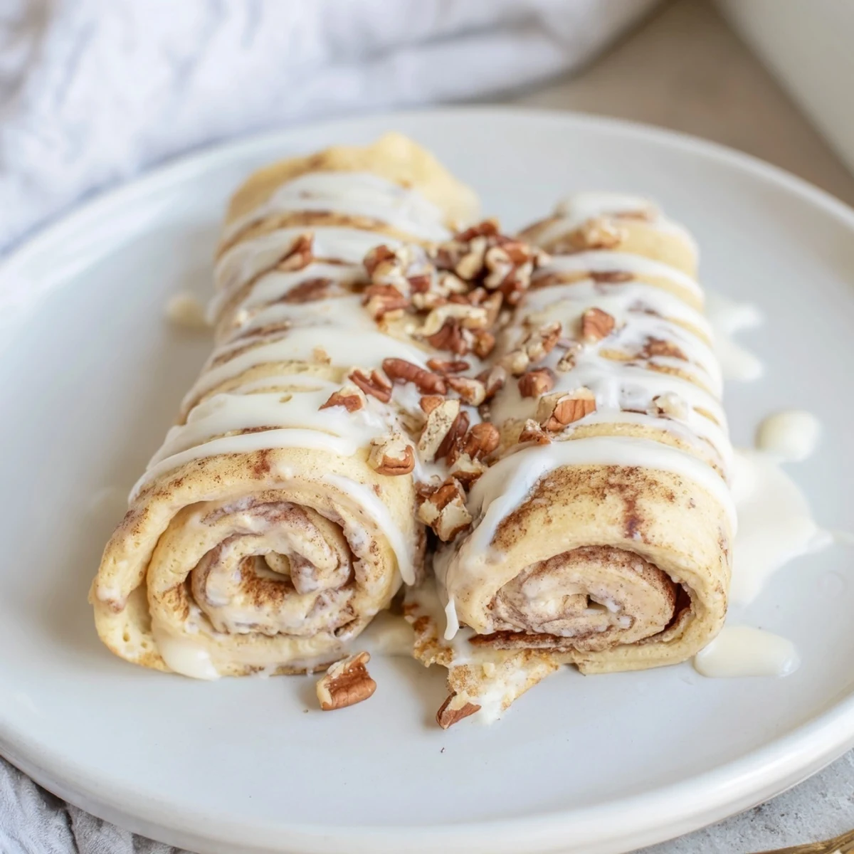 Cinnamon Roll Protein Crepes drizzled with sweet vanilla glaze on a warm plate