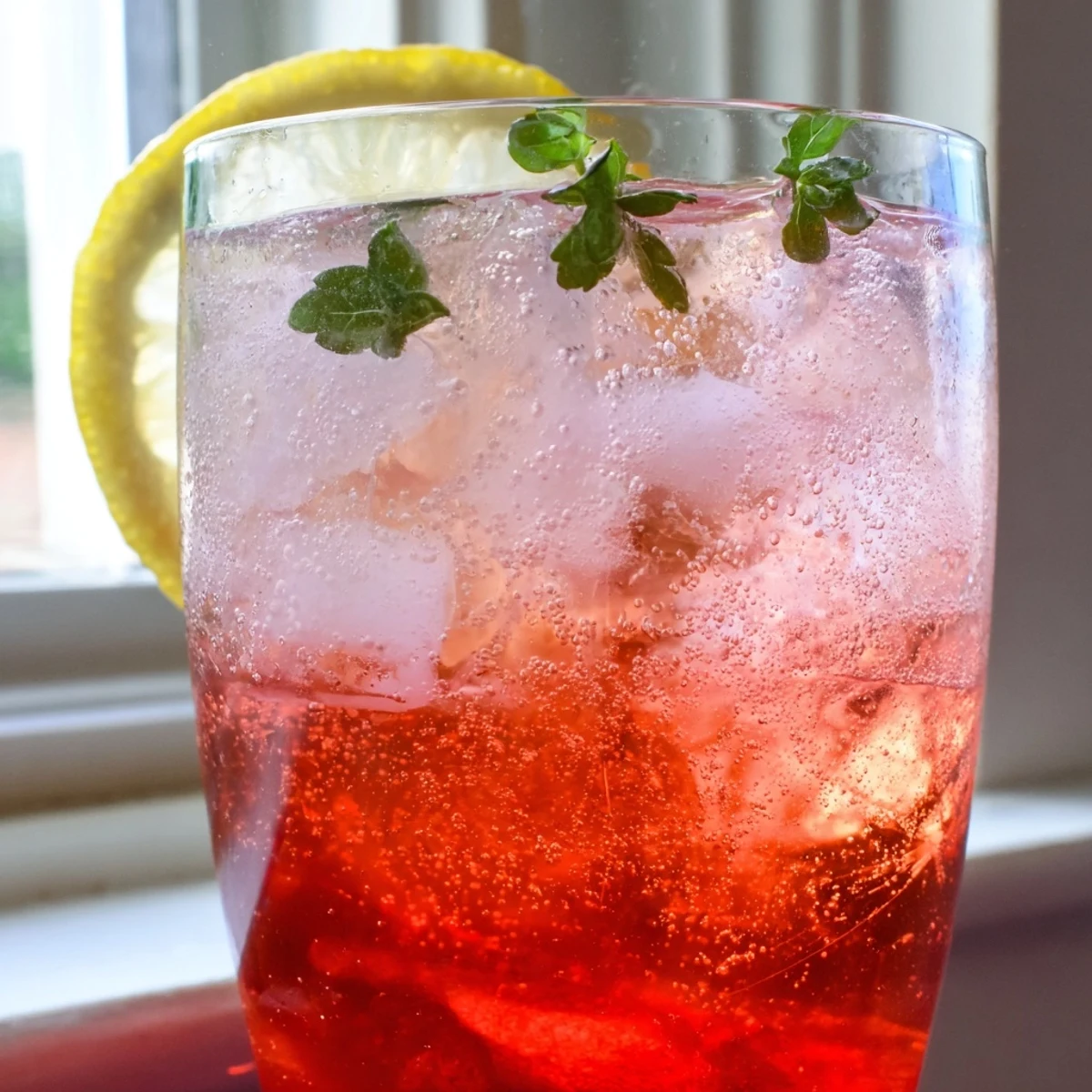 Two tall glasses of honey lemon pink soda topped with citrus wheels and mint