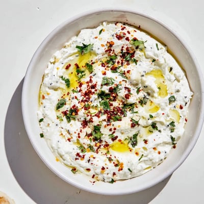 Bright Greek Tyrokafteri dip in a white bowl, surrounded by crisp veggies and warm pita wedges for dipping.