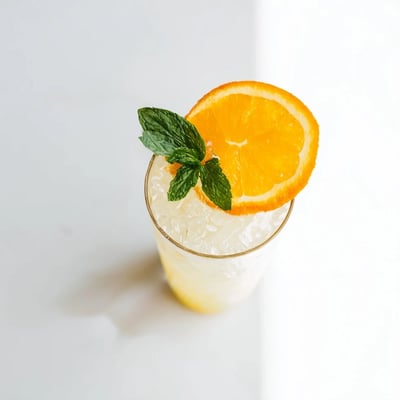 A close-up of ice cubes in Refreshing Coconut Orange Glow beverage, highlighting fresh orange and mint garnish.