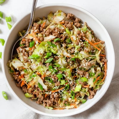 A generous bowl of keto egg roll in a bowl loaded with shredded carrots, green onions, and savory seasoned meat.