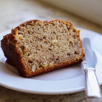 Warm slice of Nana's Secret Banana Nut Bread topped with melting butter on a plate