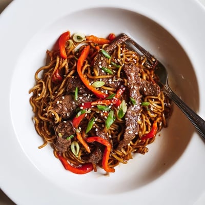 Bowl of Sticky Beef Noodles steaming, chewy strands, bright bell pepper slices